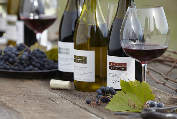 Several bottles of Davis Bynum on a wooden table near plates of grapes